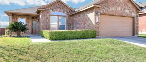 A two-story brick house with a garage, a front door, and a small front yard with a hedge.