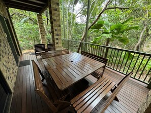 A wooden deck with a table and benches, surrounded by a railing and lush greenery.