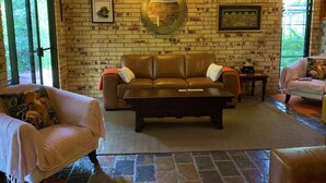 A living room with a brick wall, a round mirror, a brown leather sofa, and two armchairs. - Avalon in Arcadia Magnetic Island (Arcadia)