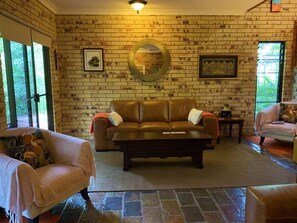 A living room with a brick wall, a round mirror, a brown leather sofa, and two armchairs.