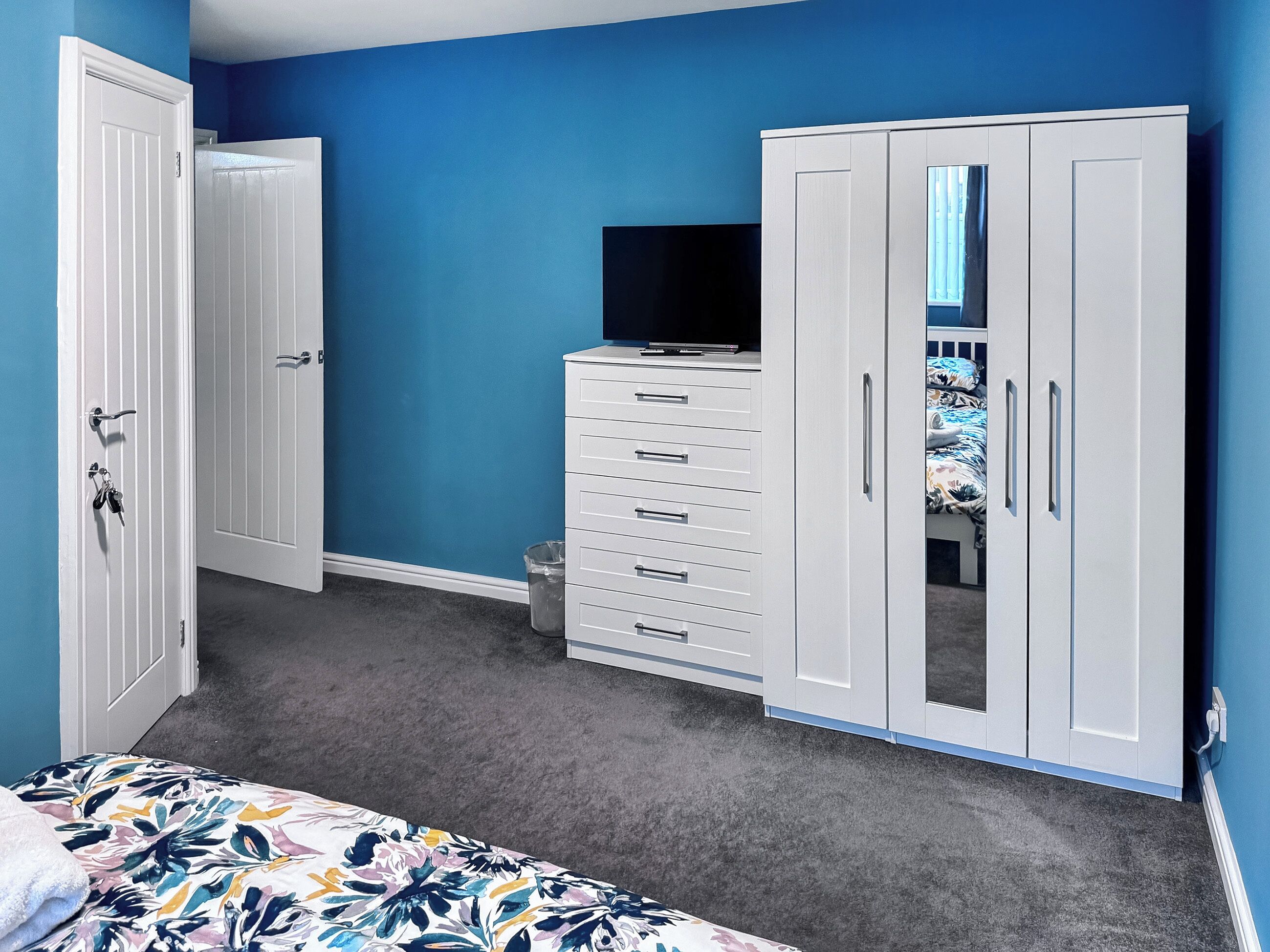 Een slaapkamer met een bed, een dressoir, een televisie en een kledingkast.