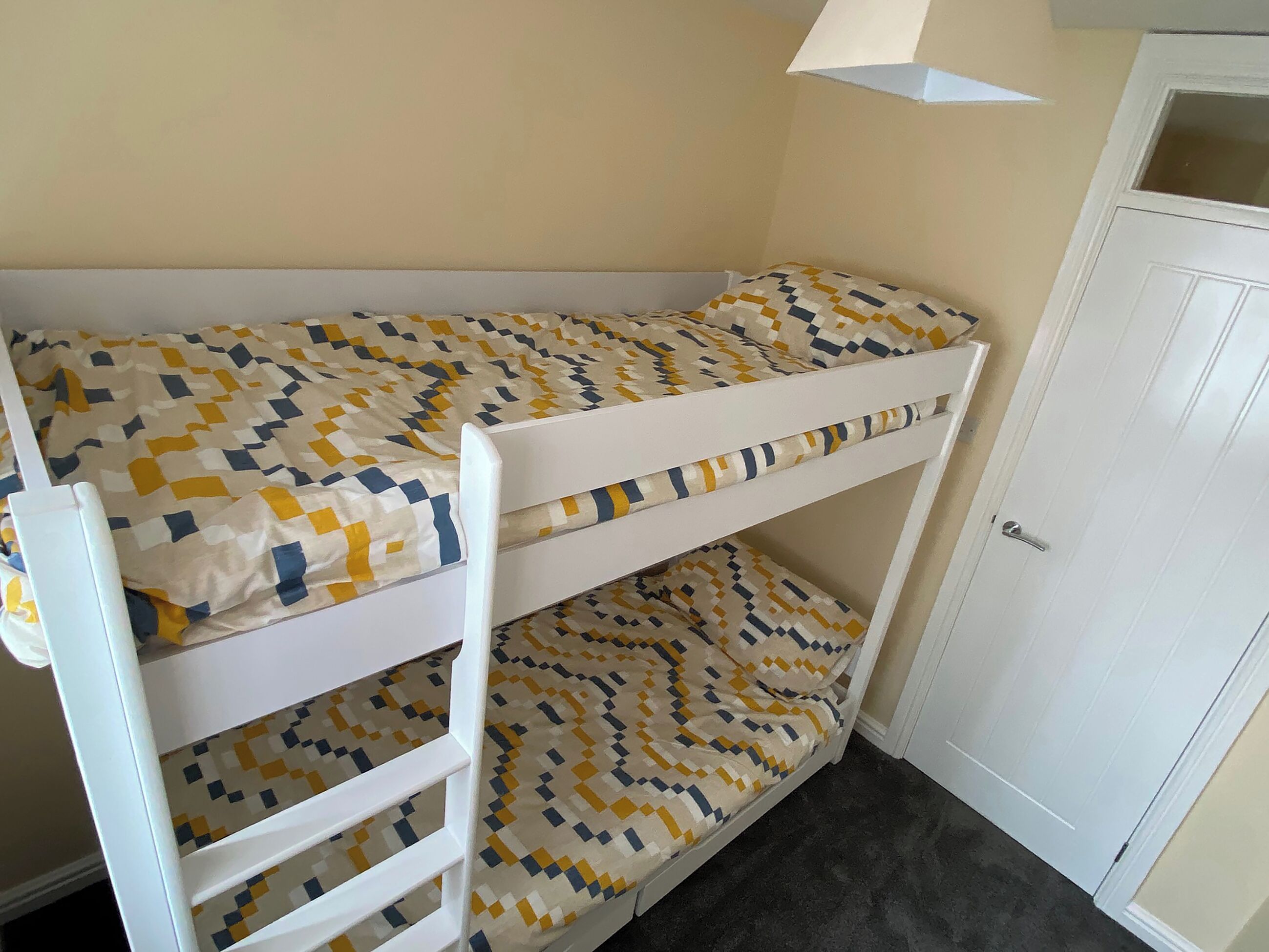 En køjeseng med et sengetæppe med geometrisk mønster i gule og blå farver.
