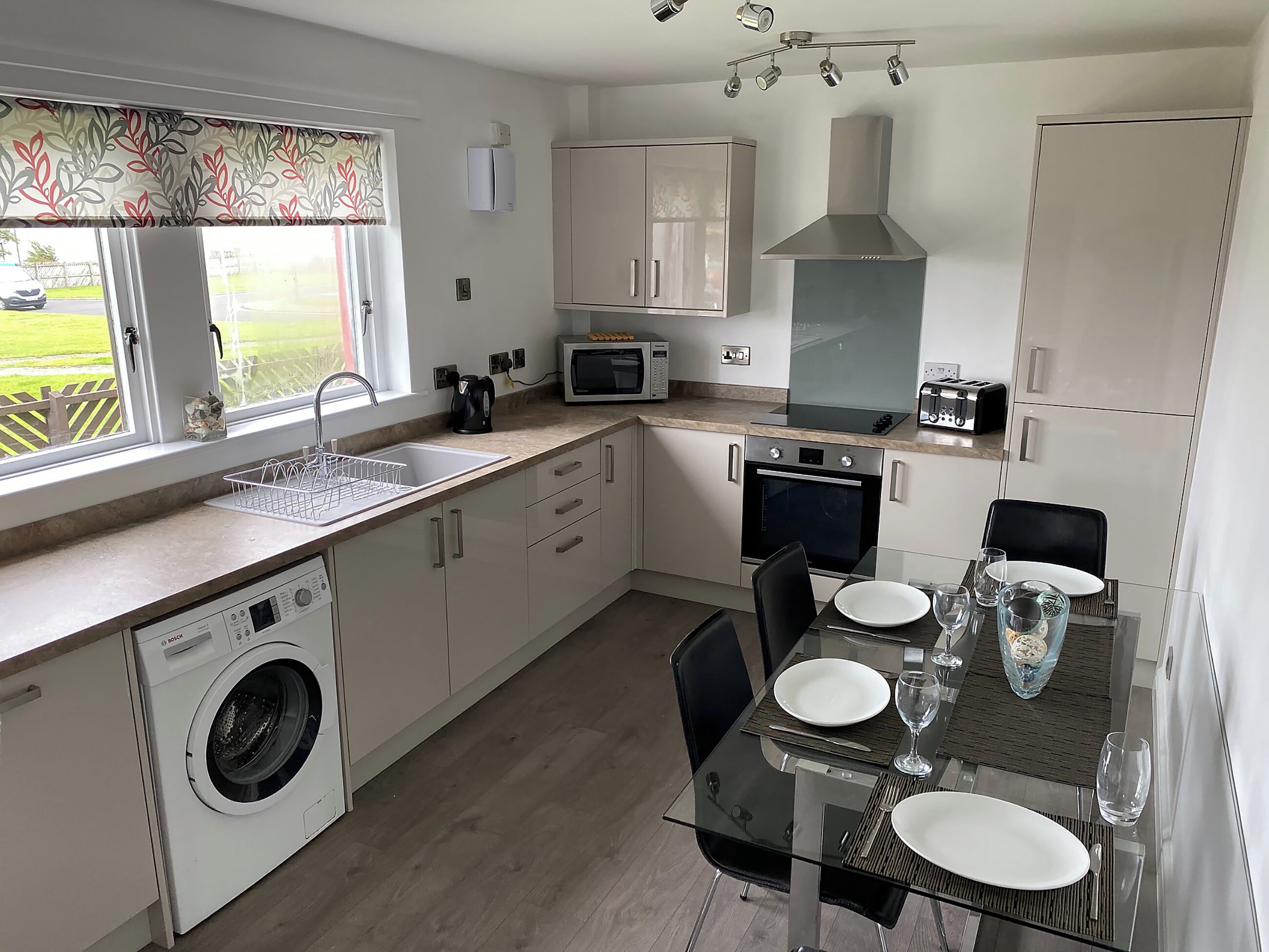 A compact kitchen with a washing machine, microwave, oven, and a dining area with a table set for two.