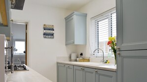 A kitchen with light blue cabinets, a white countertop, a sink, and a window with blinds.