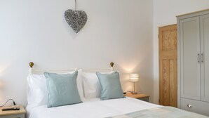 A neatly made bed with a white and blue checkered bedspread, a heart-shaped wall decoration, and a wooden wardrobe.