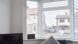A room with a television on a wooden shelf, a laptop on the windowsill, and a blue chair with a striped pillow.