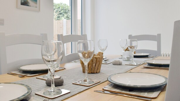A dining table set with plates, glasses, and cutlery, with a view of the outdoors through a window.