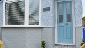 A house with a blue door, a small garden, and a number 65 sign.