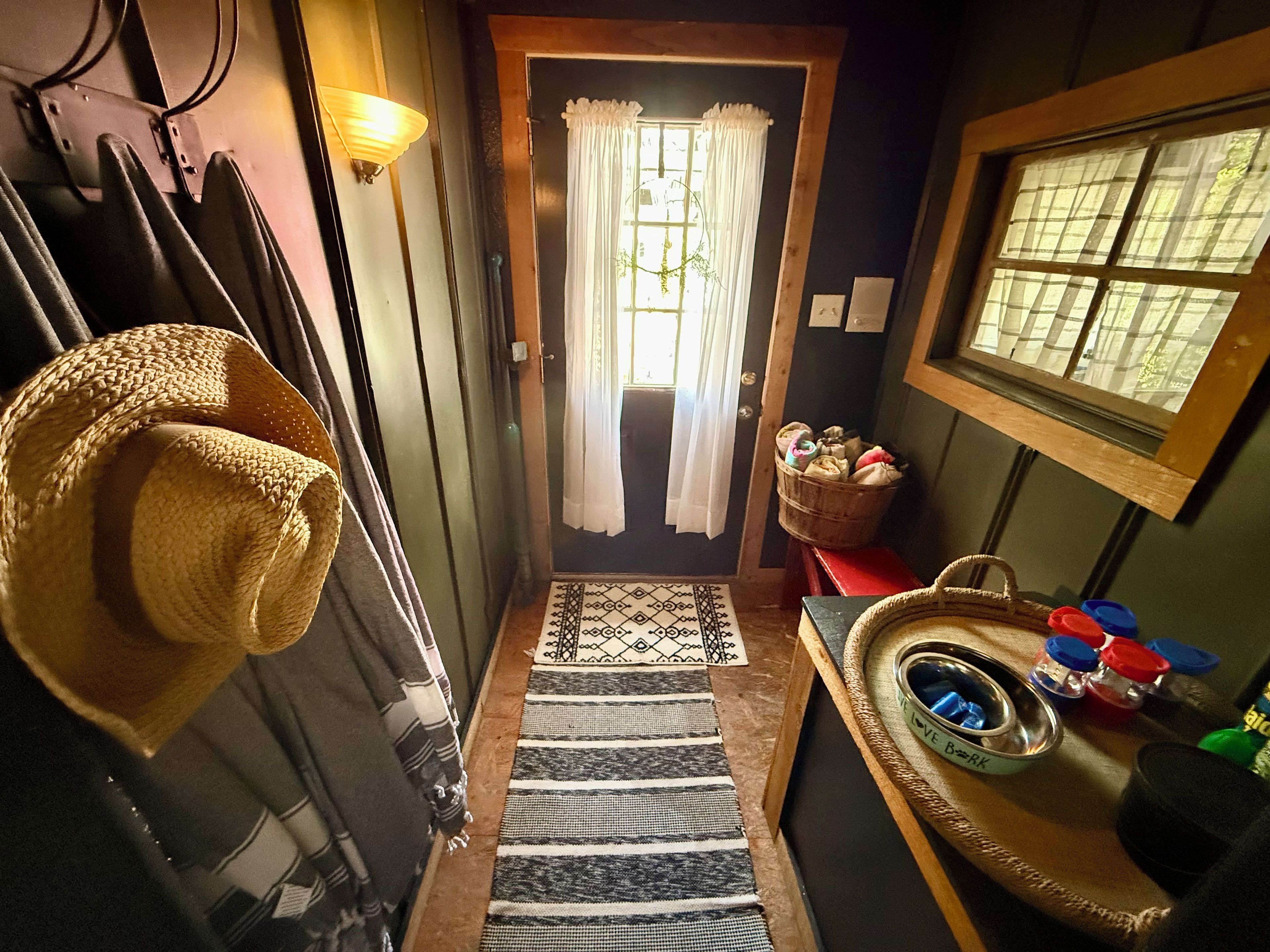 A hallway with a straw hat hanging on the wall, a basket of toiletries, and a window with a view.