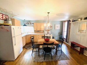 A compact kitchen with a dining area, wooden cabinets, a white refrigerator, and a chandelier. - Cottage with Hot Tub & Pool in Texas Hill Country  (Bandera)