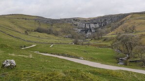 Un paysage rural avec un mur de pierres, un sentier et un petit ruisseau.