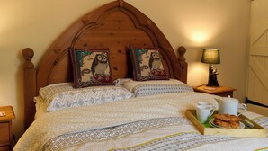 Un lit bien fait, avec une literie à motifs, deux coussins décoratifs, une table de chevet avec une lampe et un plateau contenant des croissants et une tasse.
