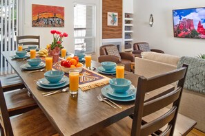 Un comedor con una mesa de madera preparada para el desayuno, vajilla azul y un frutero.