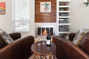 A living room with leather sofas, a small wooden table with a wine bottle and glasses, a fireplace, and a shelf with decorative items. - EL Altos and The Plaza - 2 Homes 1 Property (Albuquerque)