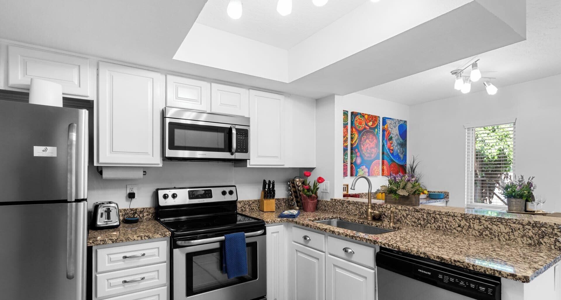 A modern kitchen with white cabinetry, stainless steel appliances, granite countertops, and a skylight.
