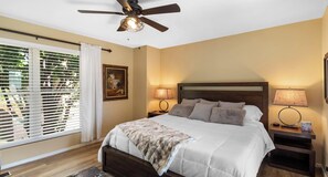 A bedroom with a bed, two bedside tables, a ceiling fan, and a window with blinds.