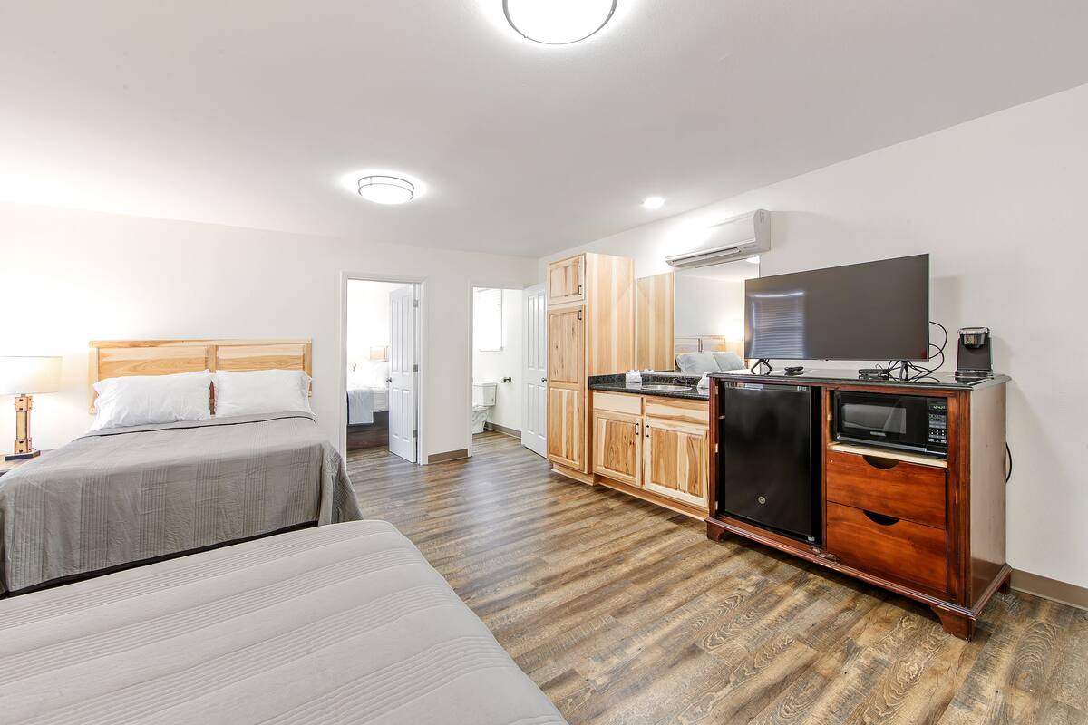 A hotel room with two beds, a kitchenette, a television, and a bathroom visible through an open door.