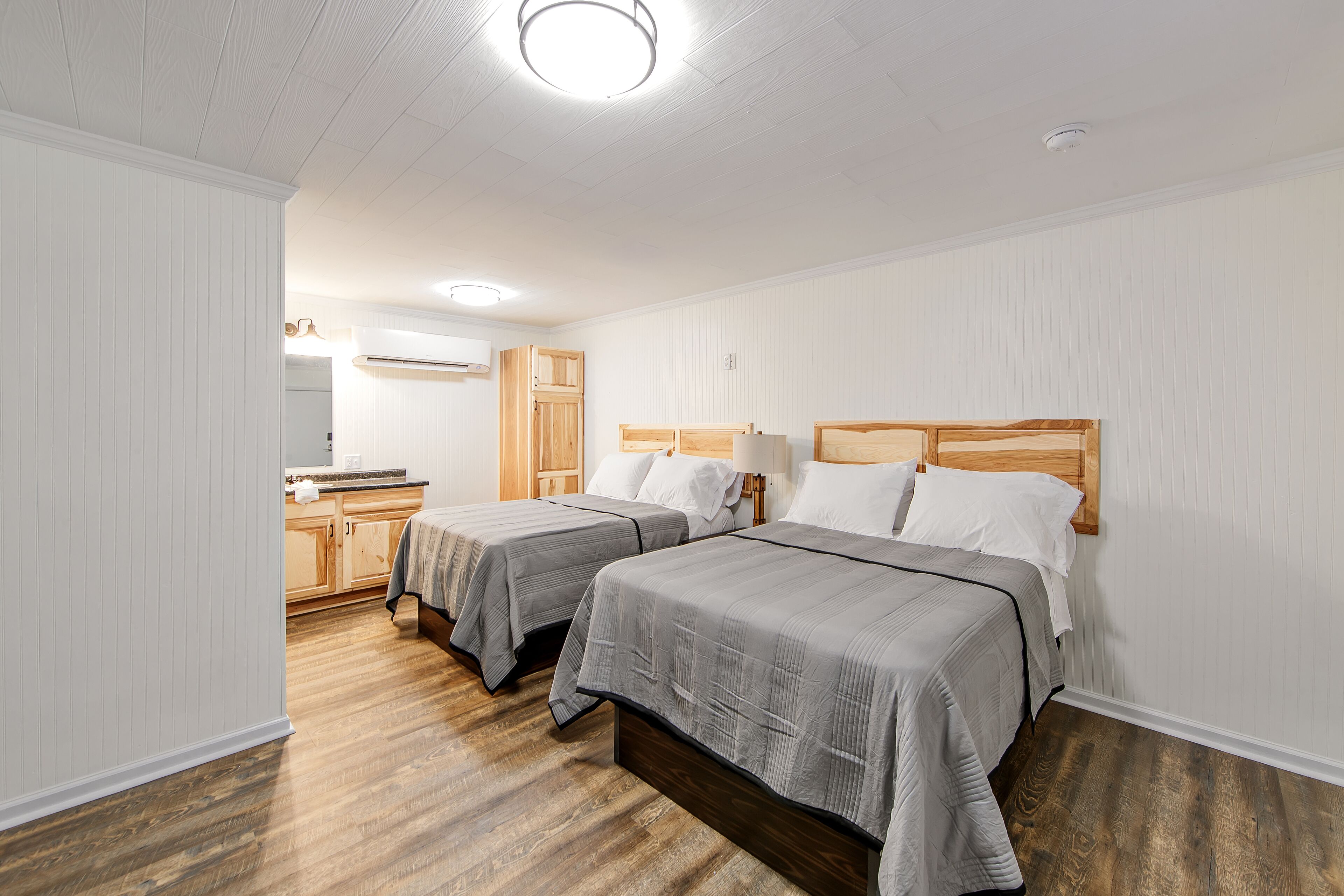 A bedroom with two beds, wooden headboards, white walls, and a wooden floor.