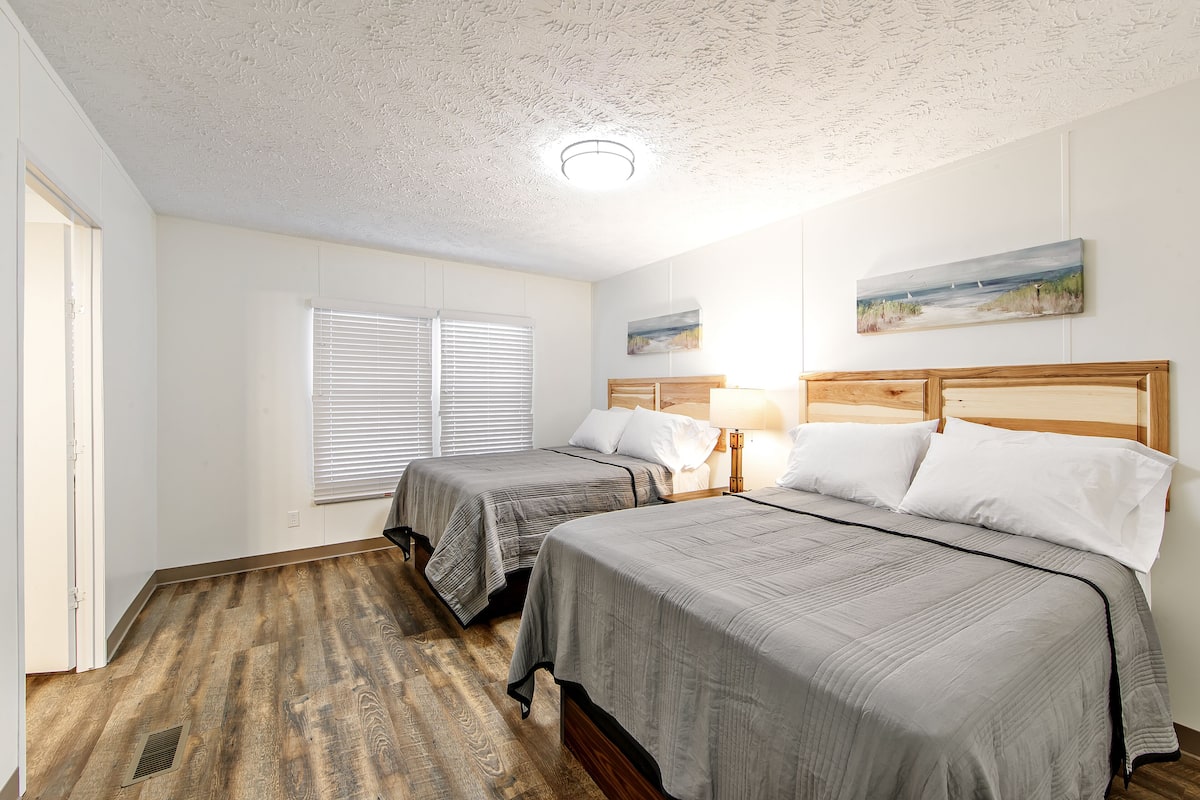A bedroom with two beds, a wooden floor, a ceiling light, and a painting on the wall.
