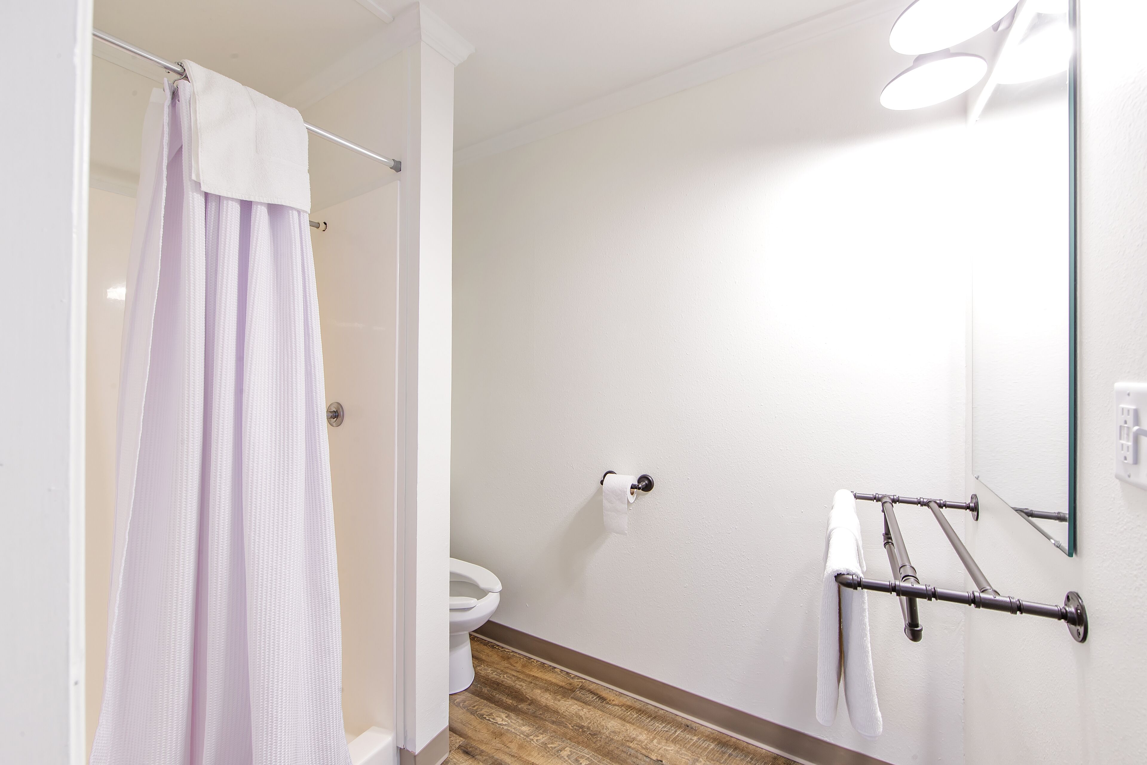 A bathroom with a shower curtain, toilet, towel rack, and a mirror.