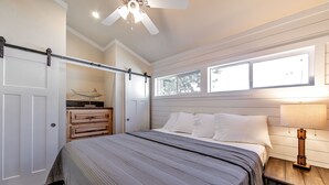 A bedroom with a bed, a nightstand, a dresser, a ceiling fan, and a window. - Southern Breeze Lodge (Golden Meadow)