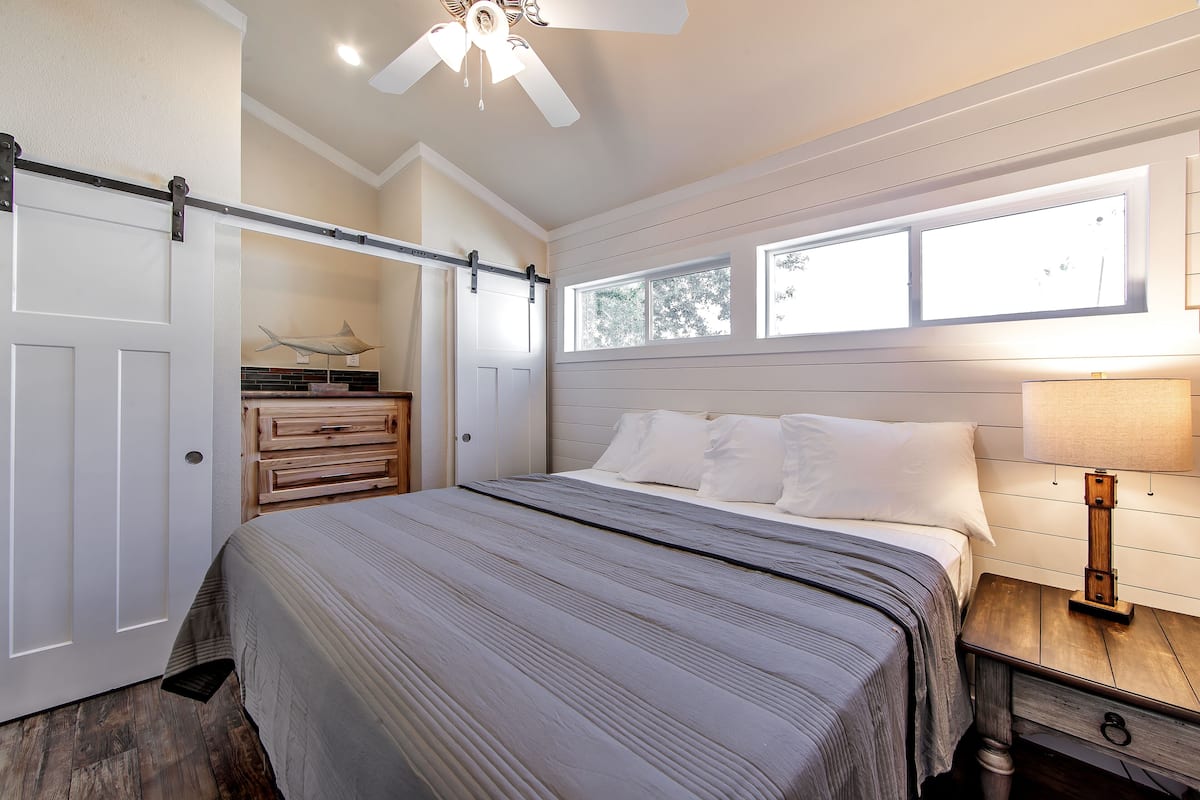 A bedroom with a bed, a nightstand, a dresser, a ceiling fan, and a window.