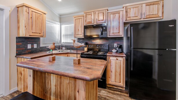 A kitchen with wooden cabinets, a black refrigerator, a microwave, and a stove. - Southern Breeze Lodge (Golden Meadow)
