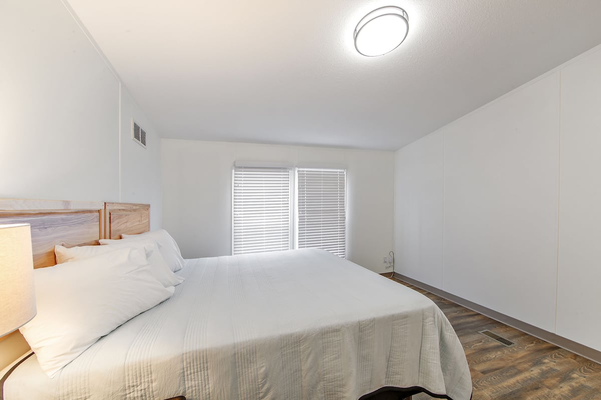 A bedroom with a bed, bedside table, and a window with blinds.