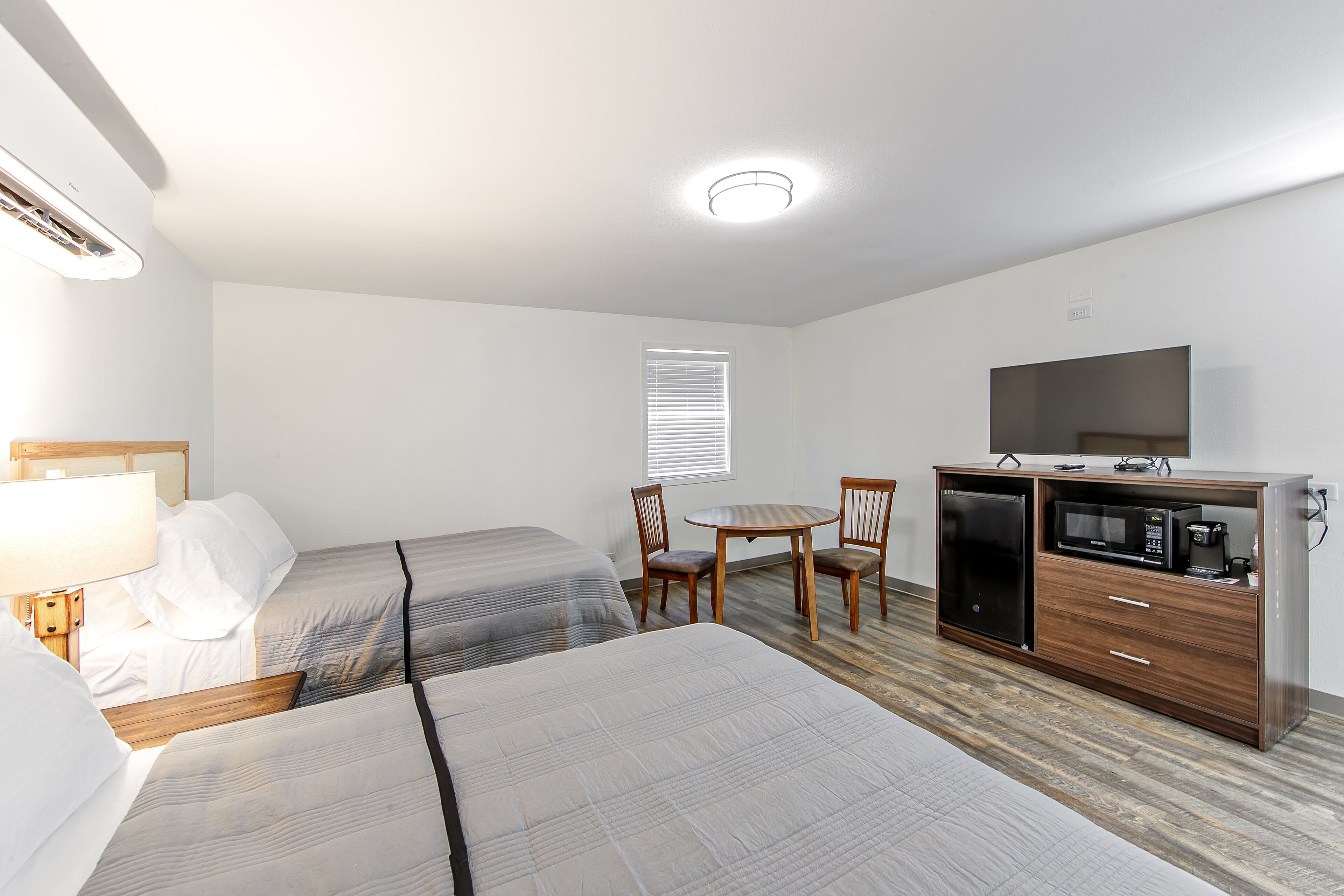 A hotel room with two beds, a desk, a chair, a microwave, a refrigerator, and a television.