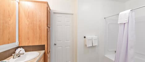 A bathroom with a wooden vanity, a white sink, a door, and a shower with a purple curtain.