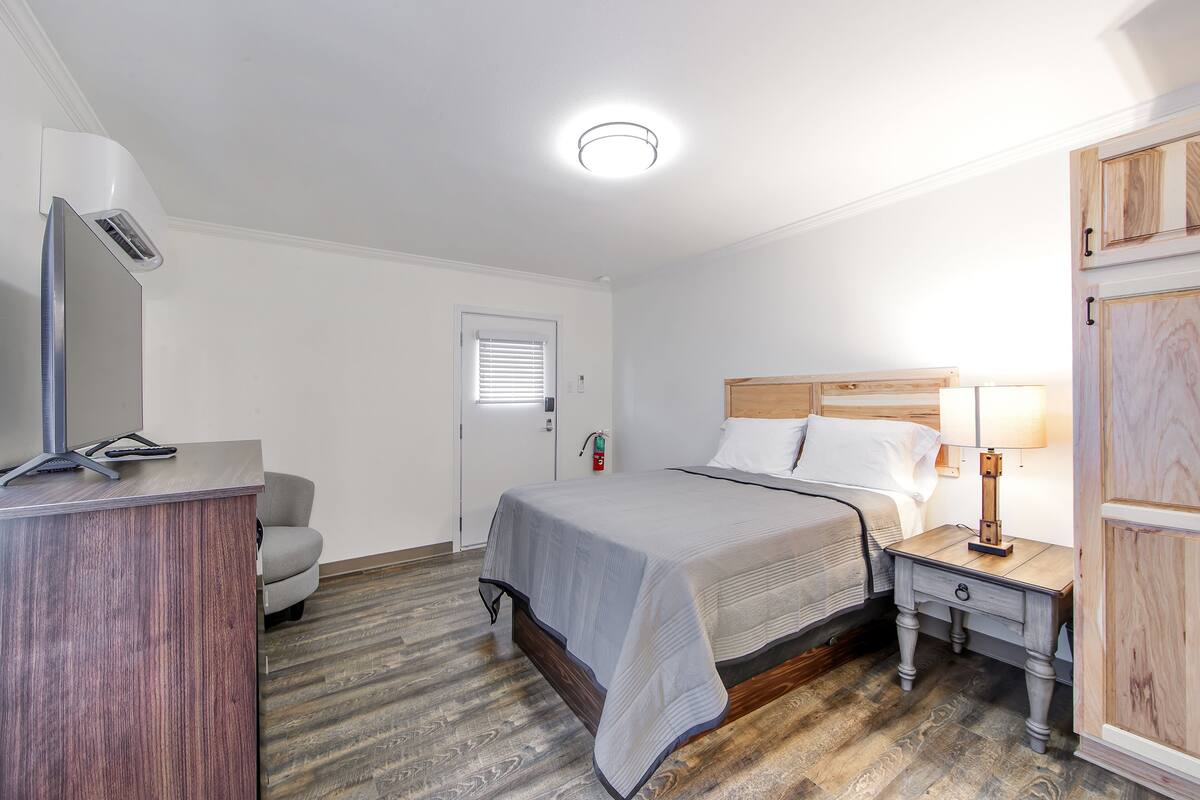 A hotel room with a bed, bedside table, lamp, and a desk with a chair.