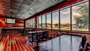 A spacious indoor area with large windows, wooden flooring, and multiple tables and chairs. - Southern Breeze Lodge (Golden Meadow)