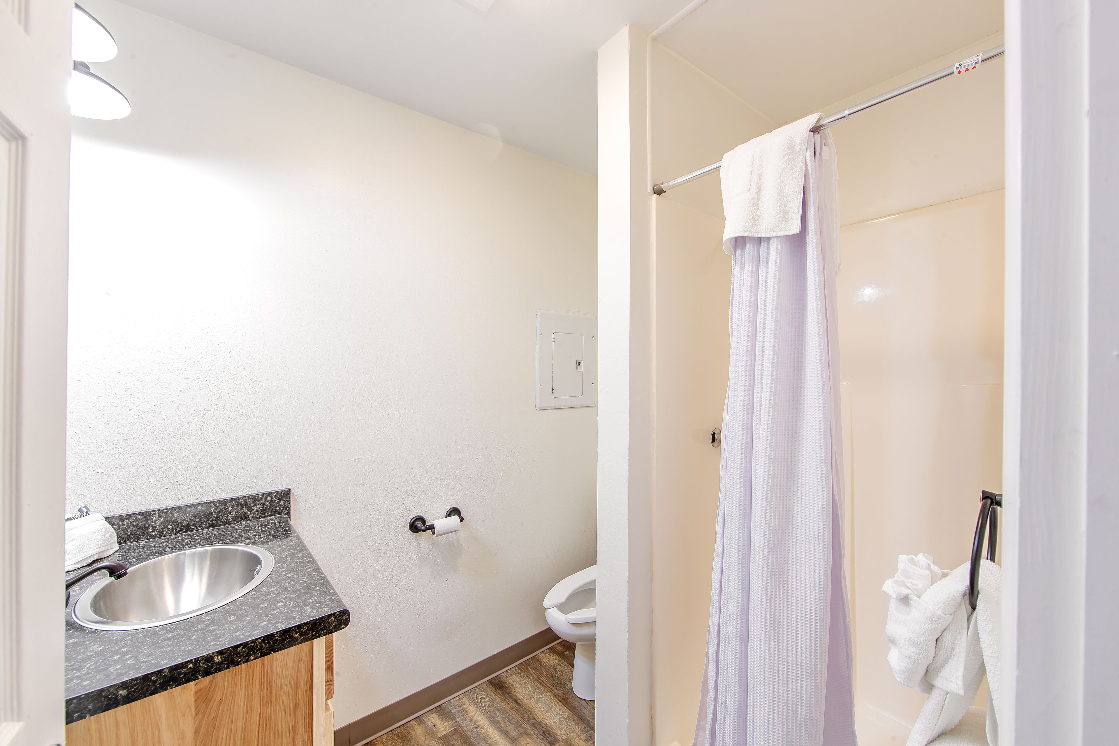 Un baño con lavamanos de encimera de granito, inodoro y ducha con cortina.
