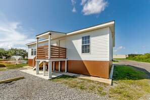 A single-story mobile home with a porch and a small deck, situated next to a gravel driveway and a grassy area. - Southern Breeze Lodge (Golden Meadow)