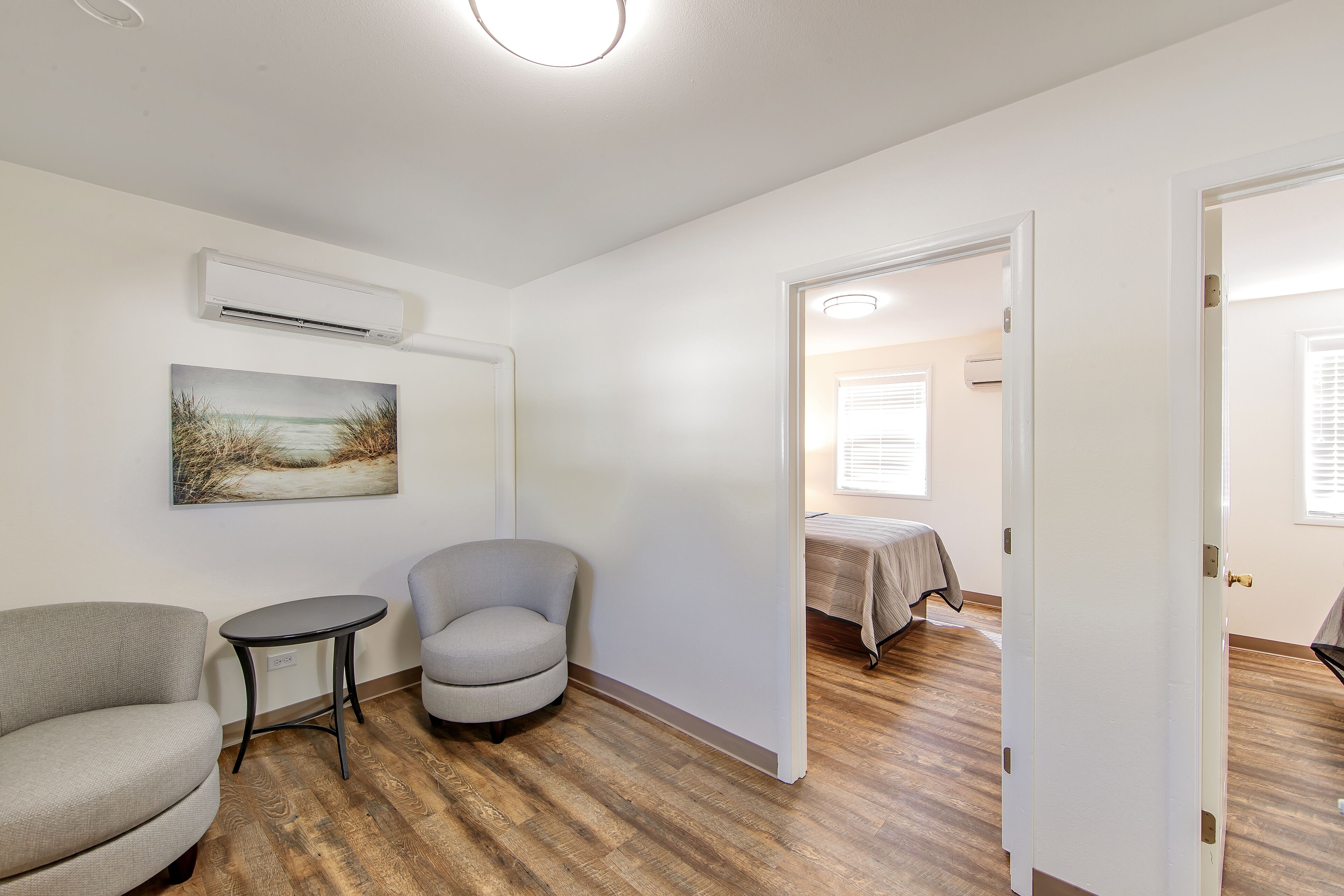 A room with a wooden floor, a gray armchair, a small round table, and a painting on the wall.