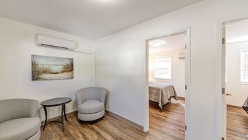 A room with a wooden floor, a gray armchair, a small round table, and a painting on the wall.