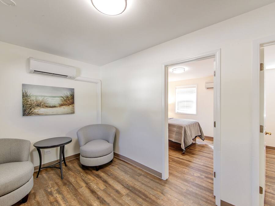 A room with a wooden floor, a gray armchair, a small round table, and a painting on the wall.