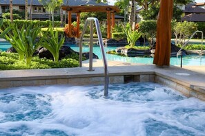 Un bain à remous entouré de plantes tropicales et un espace piscine agrémenté d’une pergola en bois.