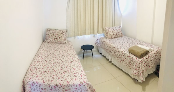 A small, clean room with two single beds, a small round table, and a window with curtains.