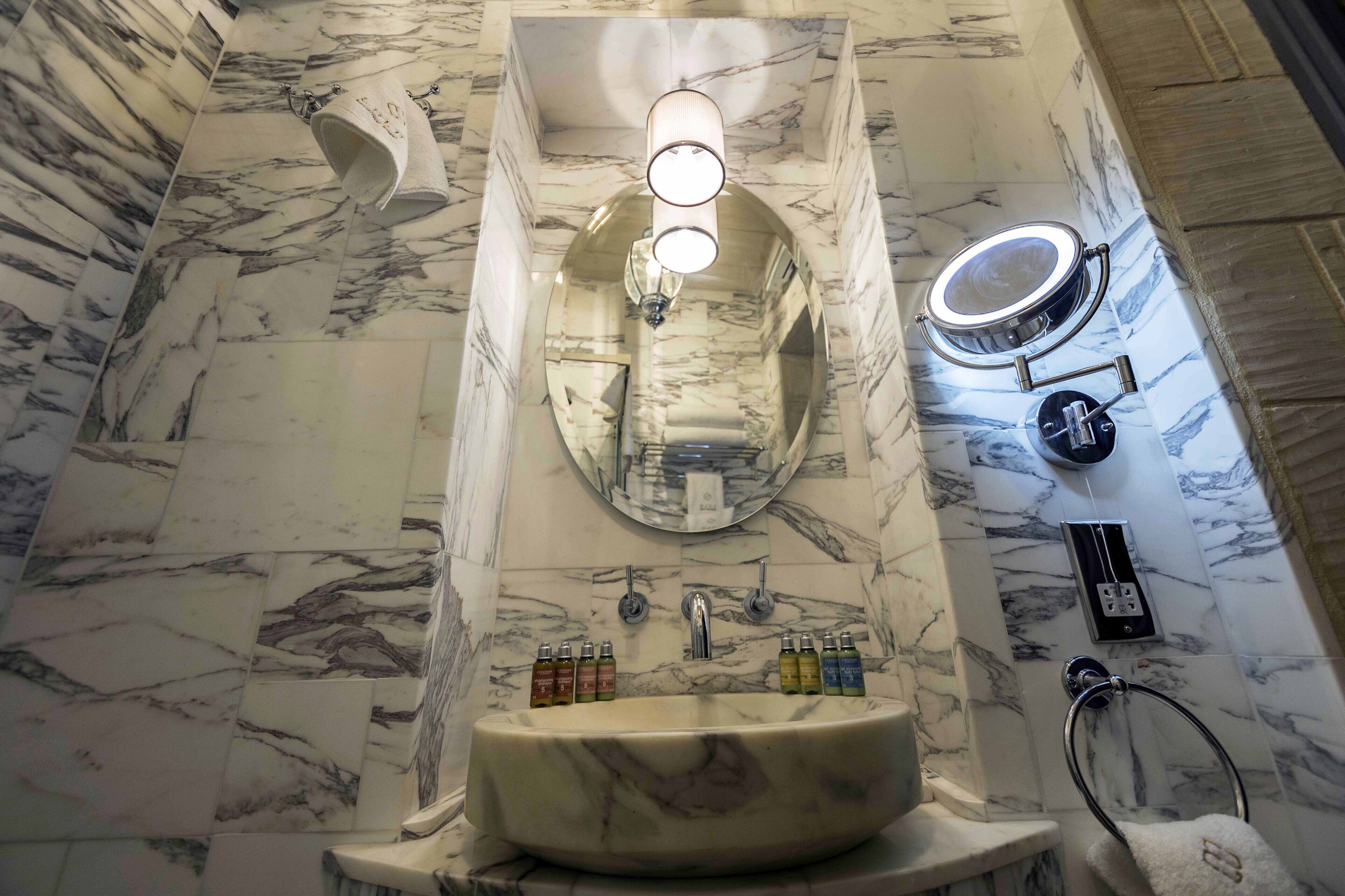 A bathroom with a marble sink, a mirror, a towel rack, and a shower area.