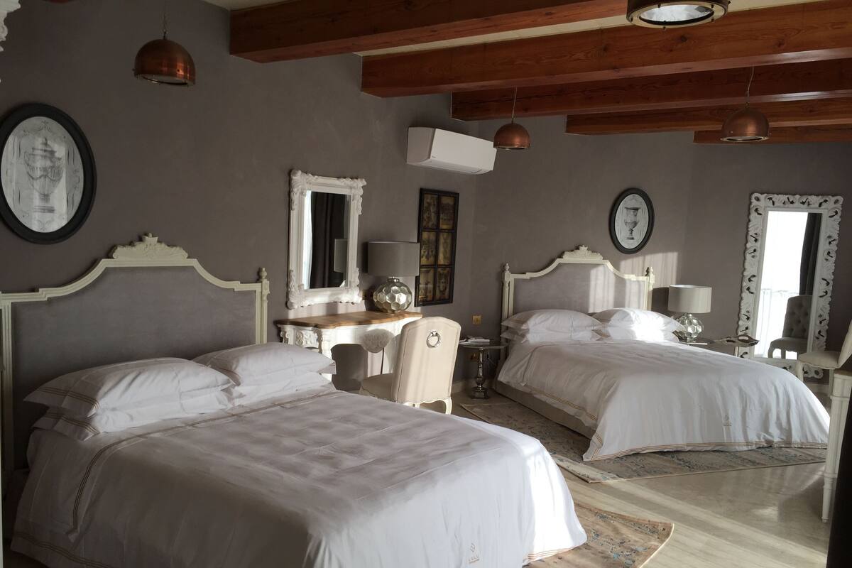 A hotel room with two beds, a desk, a chair, and a mirror.