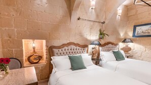 Un dormitorio con dos camas, paredes de piedra, una mesita con un florero y un cuadro en la pared.