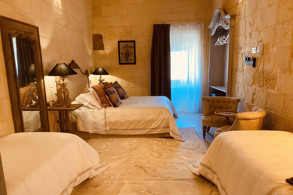 A hotel room with two beds, a sitting area with a chair, a mirror, and a picture on the wall.