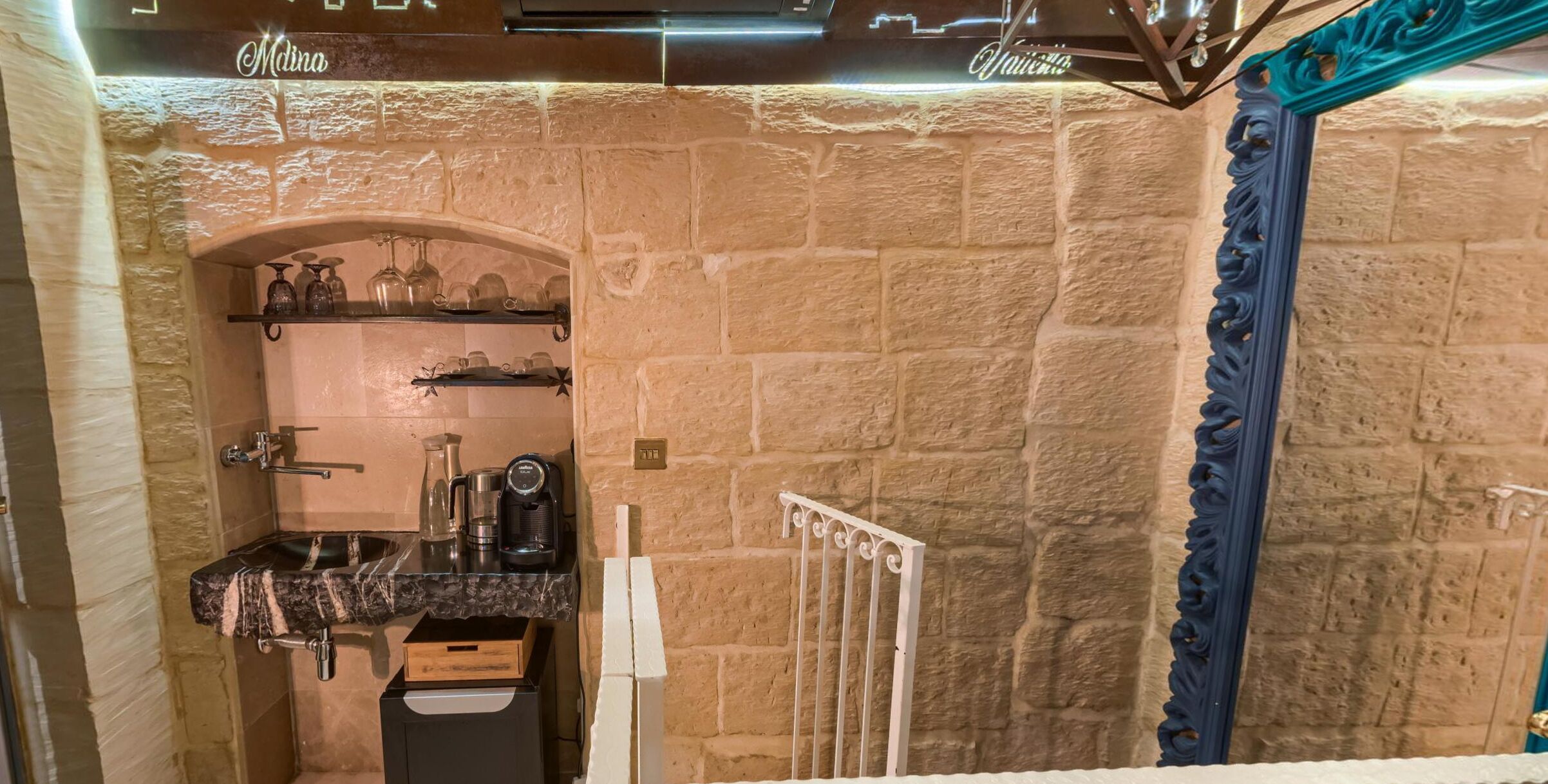 A stone-walled bathroom with a marble sink, shelves with glassware, and a decorative mirror.