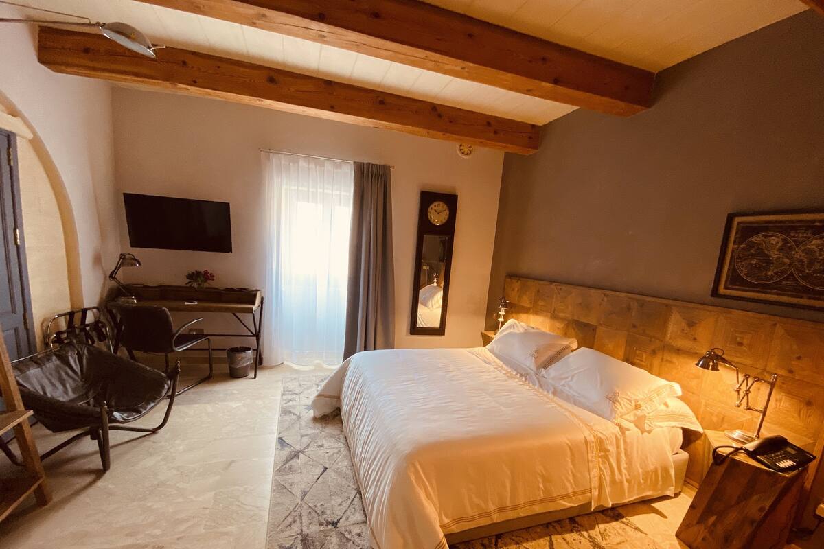 A hotel room with a bed, desk, chair, and a clock on the wall.