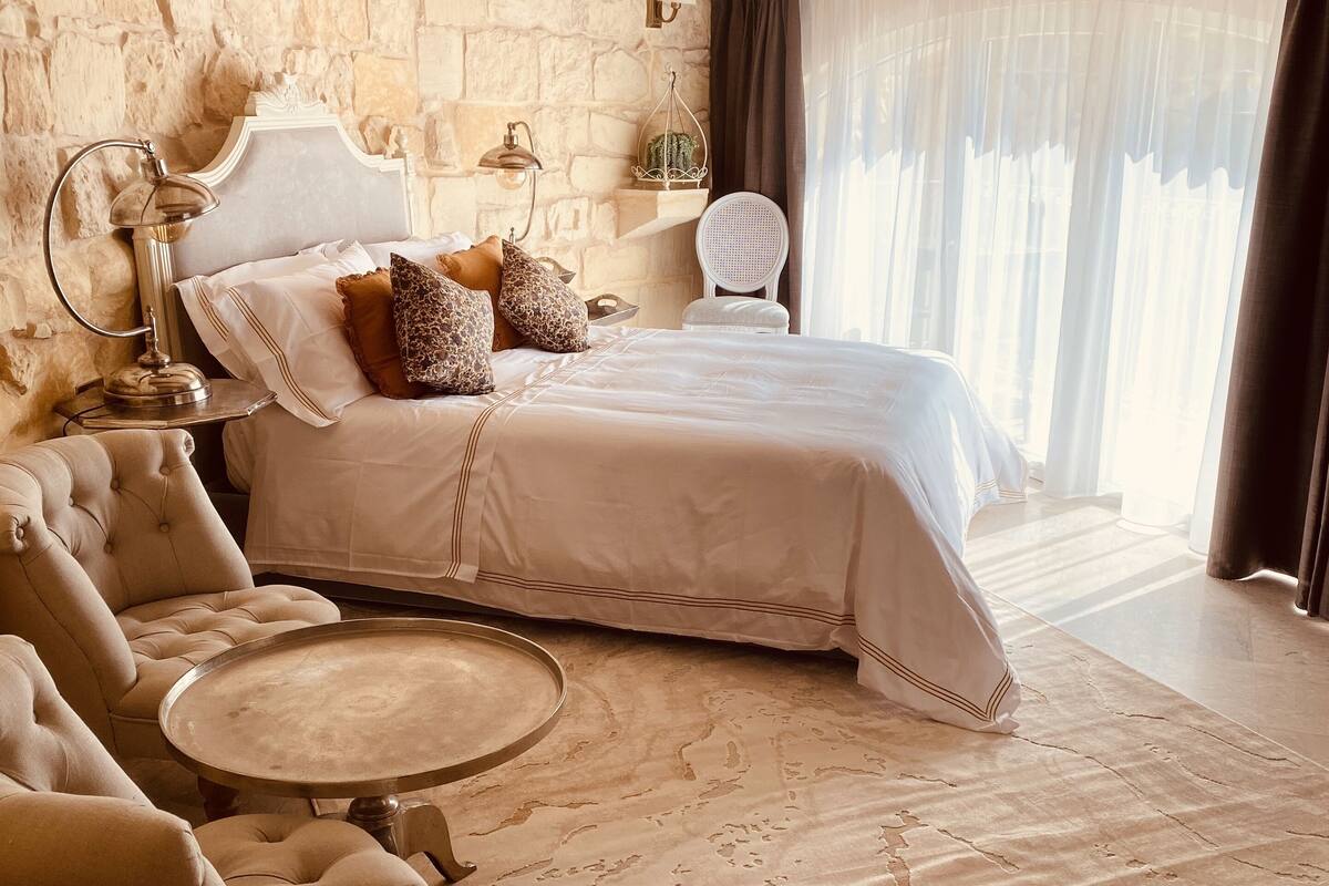 A bedroom with a large bed, a sitting area with a table, and a stone wall.