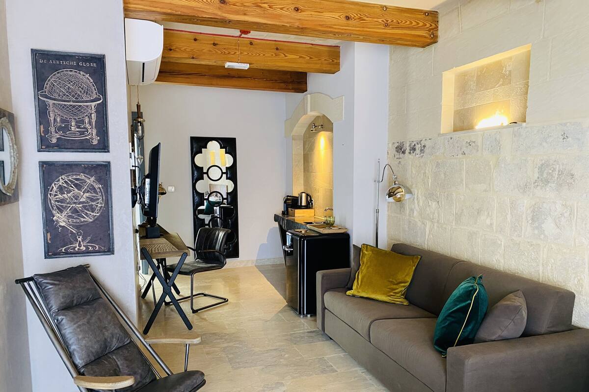 A modern living room with a brown leather sofa, a black leather chair, and a dining area with a black table and chairs.