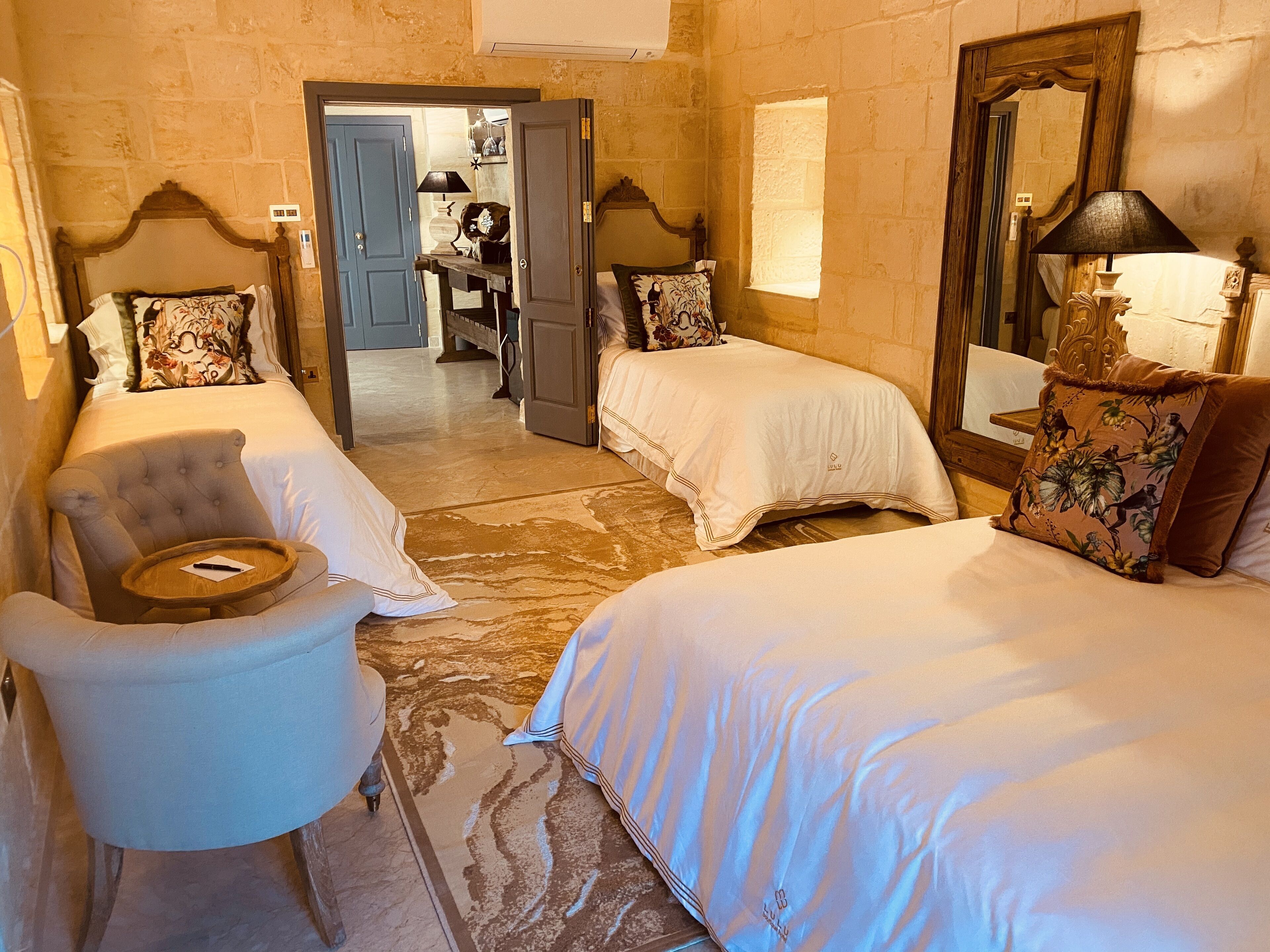 A hotel room with two beds, a chair, a small table, and a mirror.