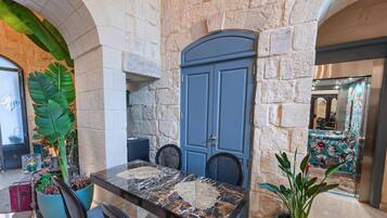 Una habitación con paredes de piedra, una puerta azul, una mesa de mármol y plantas en macetas.