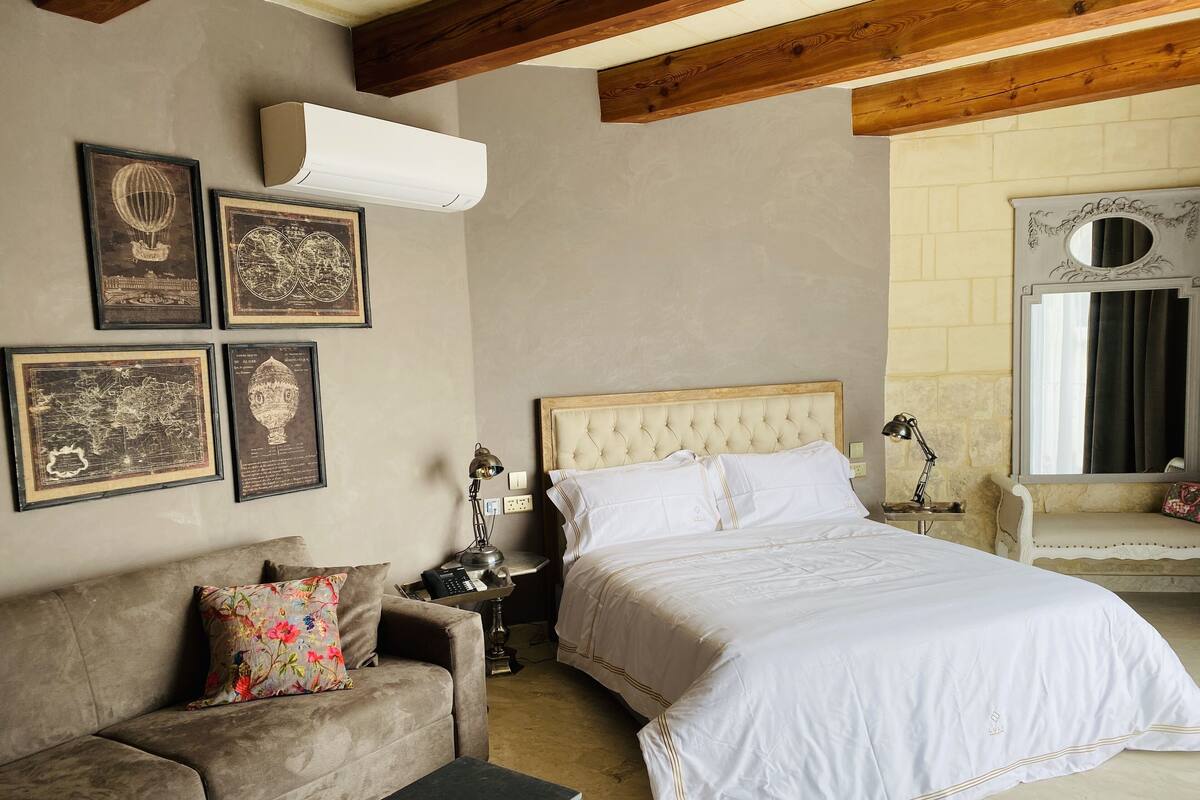 A bedroom with a bed, a sofa, a nightstand, a lamp, and wall-mounted artwork.